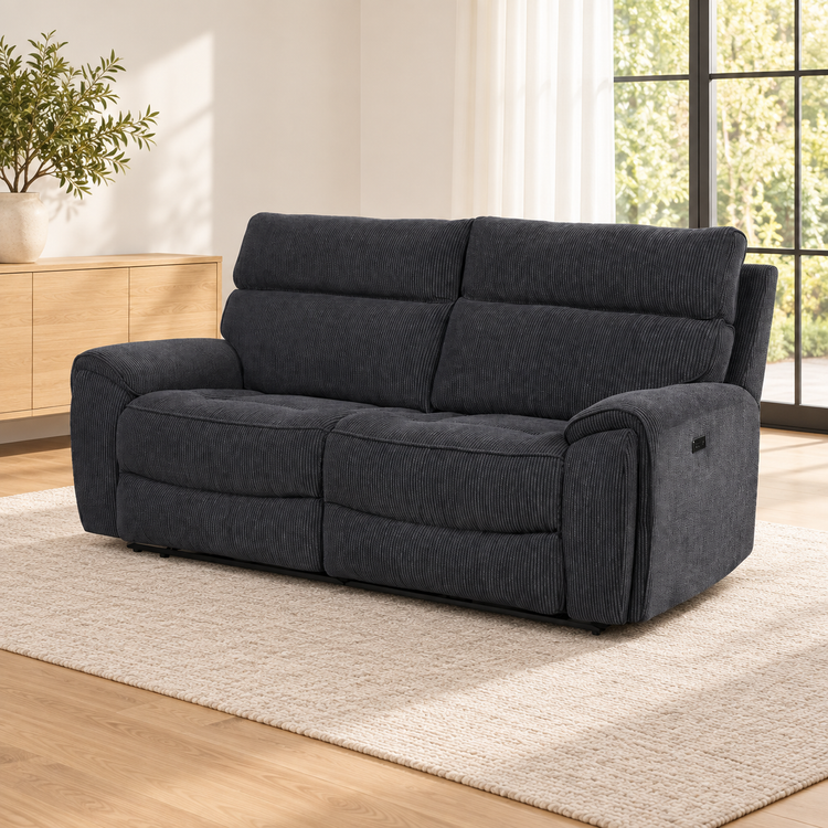 A dark charcoal gray corduroy power reclining loveseat sofa placed on a light beige textured rug in a bright, modern living room with light wood floors and a window.